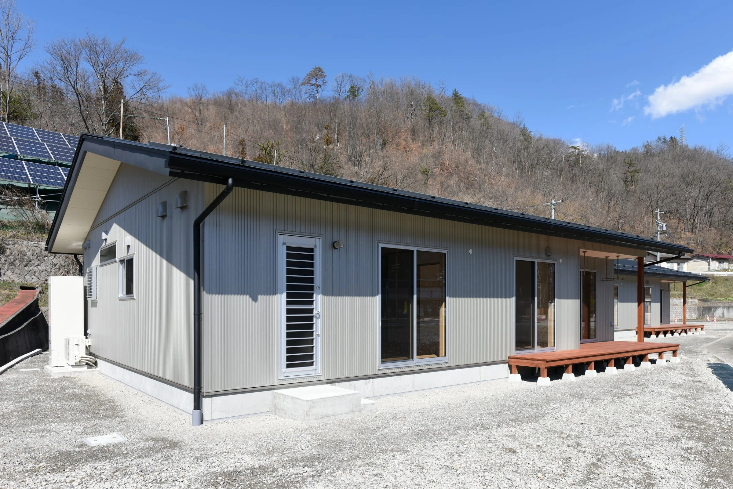 掃き出し窓が並ぶ住宅の側面と、右手のウッドデッキ