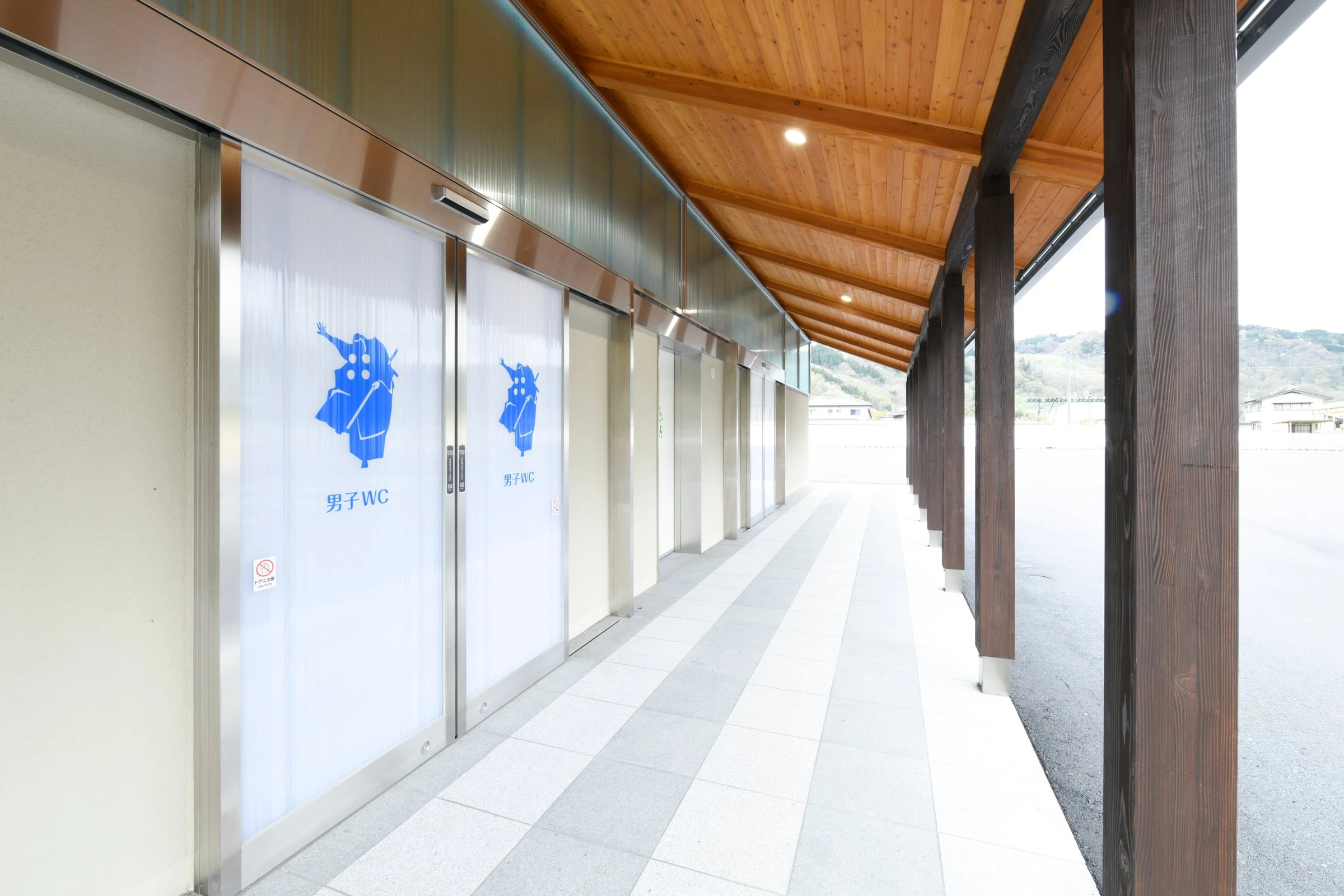 木の天井の庇の下に続く通路と、トイレの入口