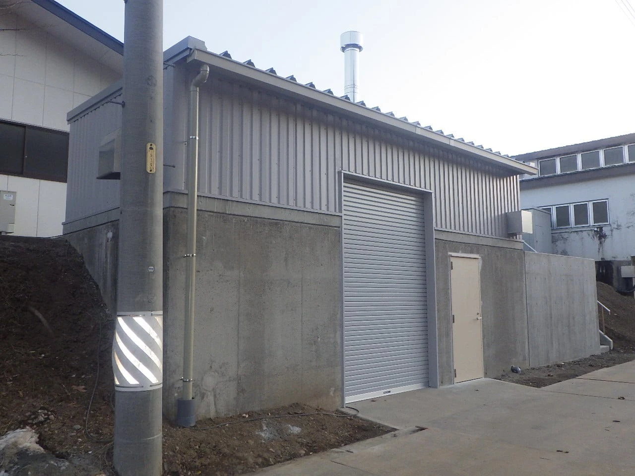 コンクリートの基礎の上に建つボイラー室。シャッターと扉が付く