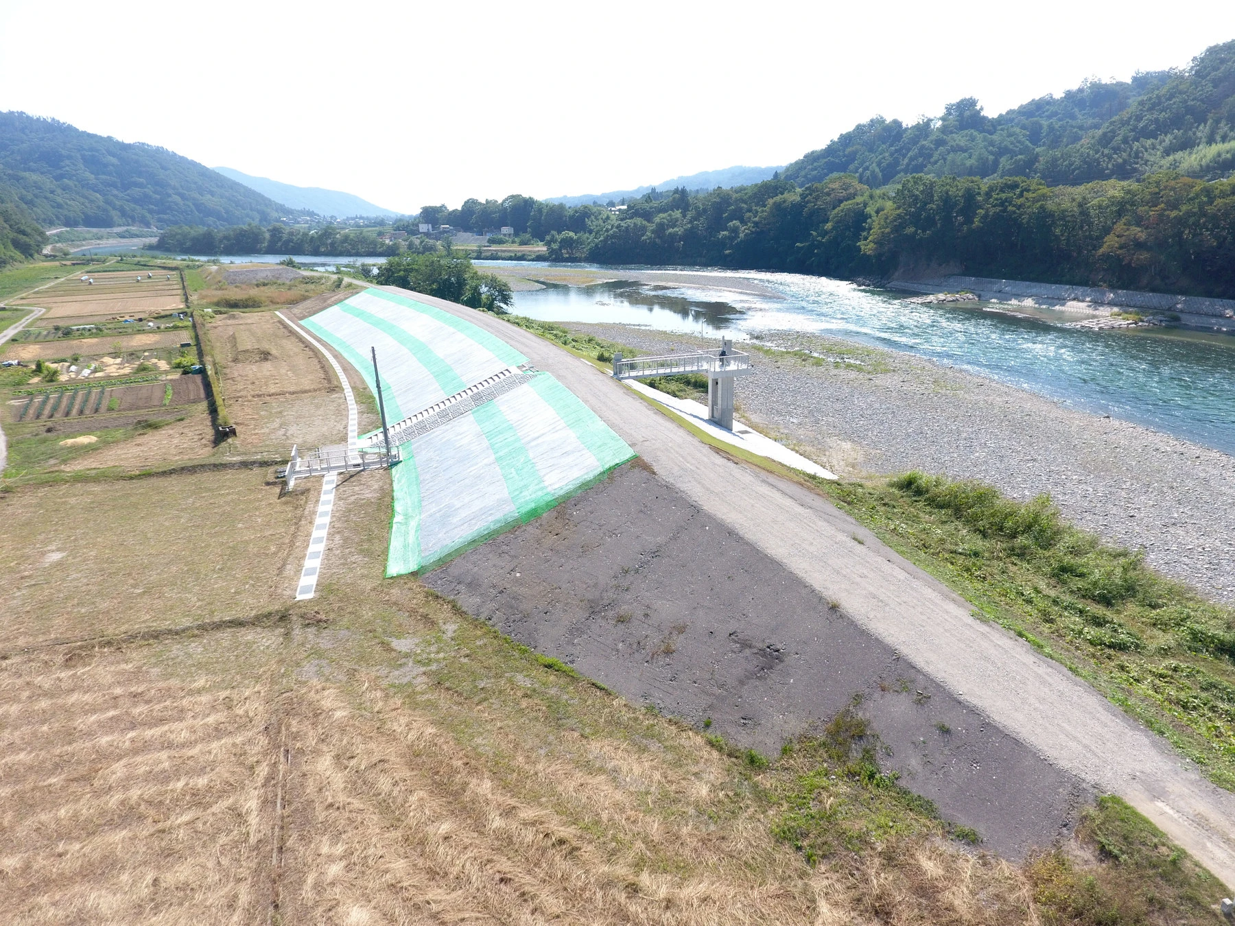 上空から見た、川沿いの堤防と、緑化した法面・その先の樋門