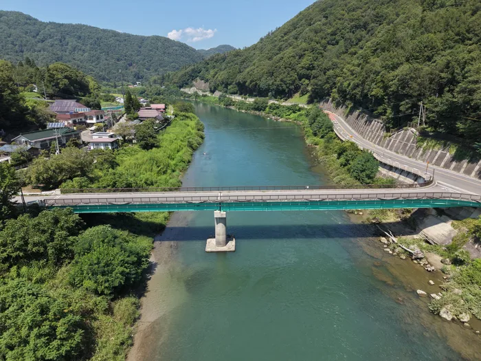 川を渡る緑色の橋を上空から見た様子。中央に橋脚が一本立つ