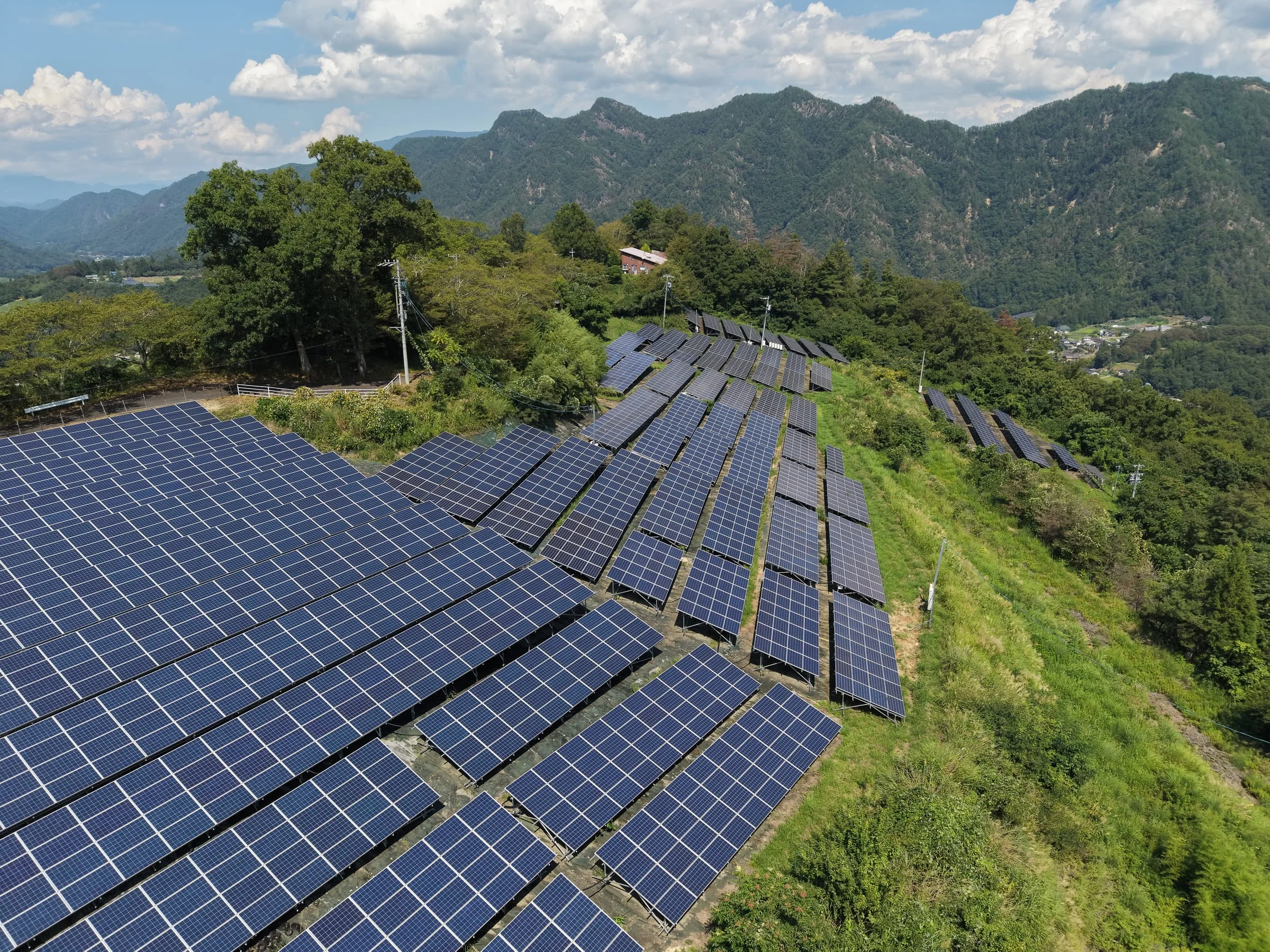 山あいの斜面に並ぶ自社保有の太陽光発電設備を上空から見たところ