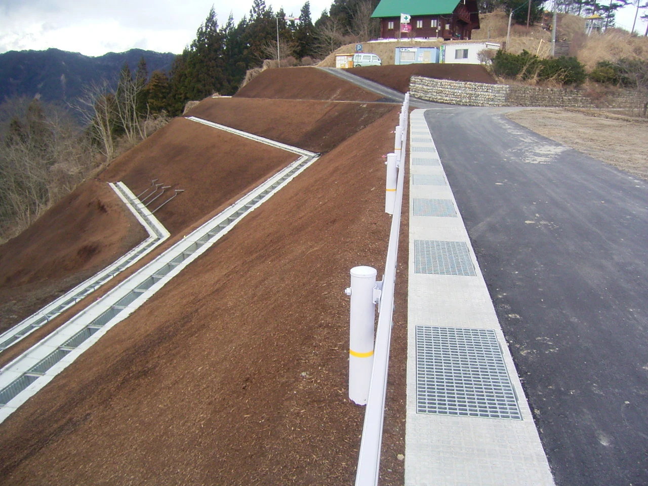 完成後、道路の上から見た法面と排水路。奥に山小屋風の建物