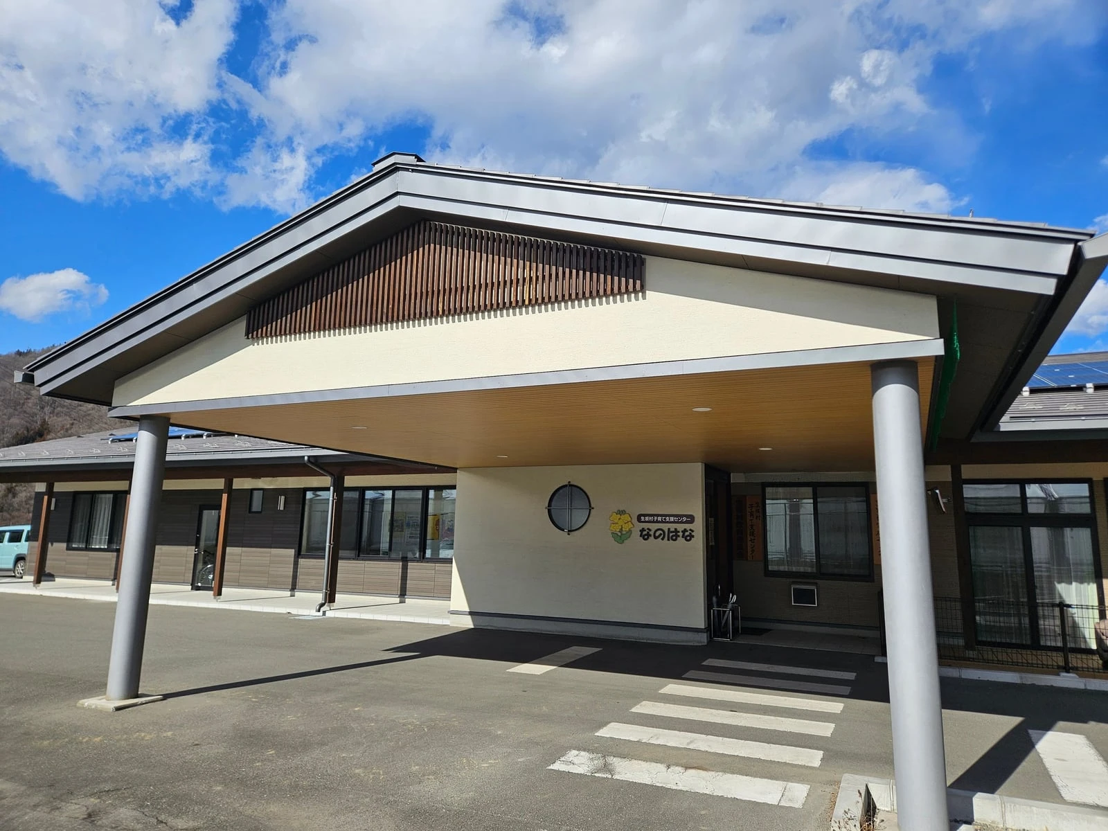 大きな切妻屋根の車寄せがある施設の正面外観