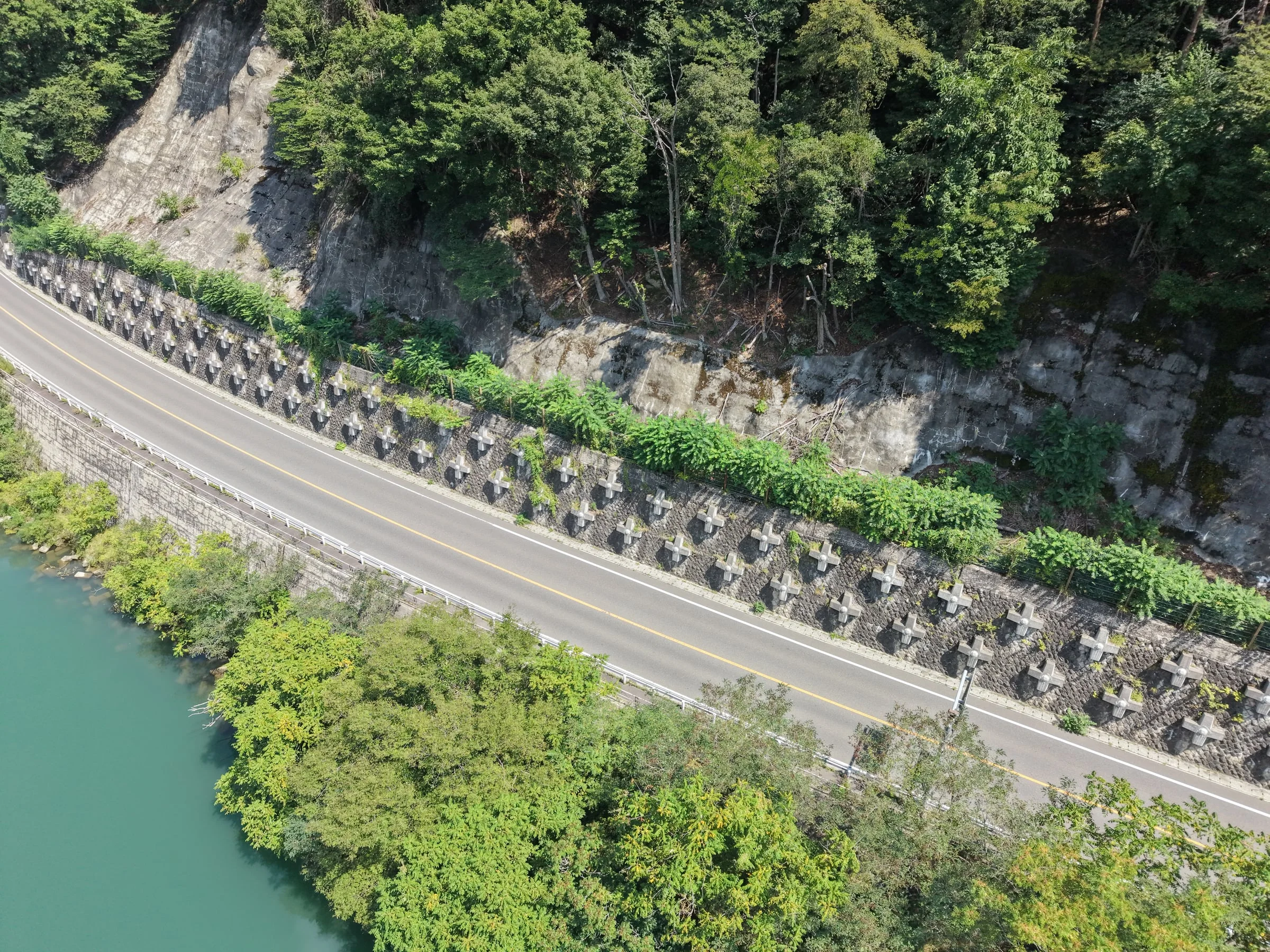 川沿いの道路脇の斜面に、十字型の受圧板が規則正しく並ぶ様子を上空から見たところ